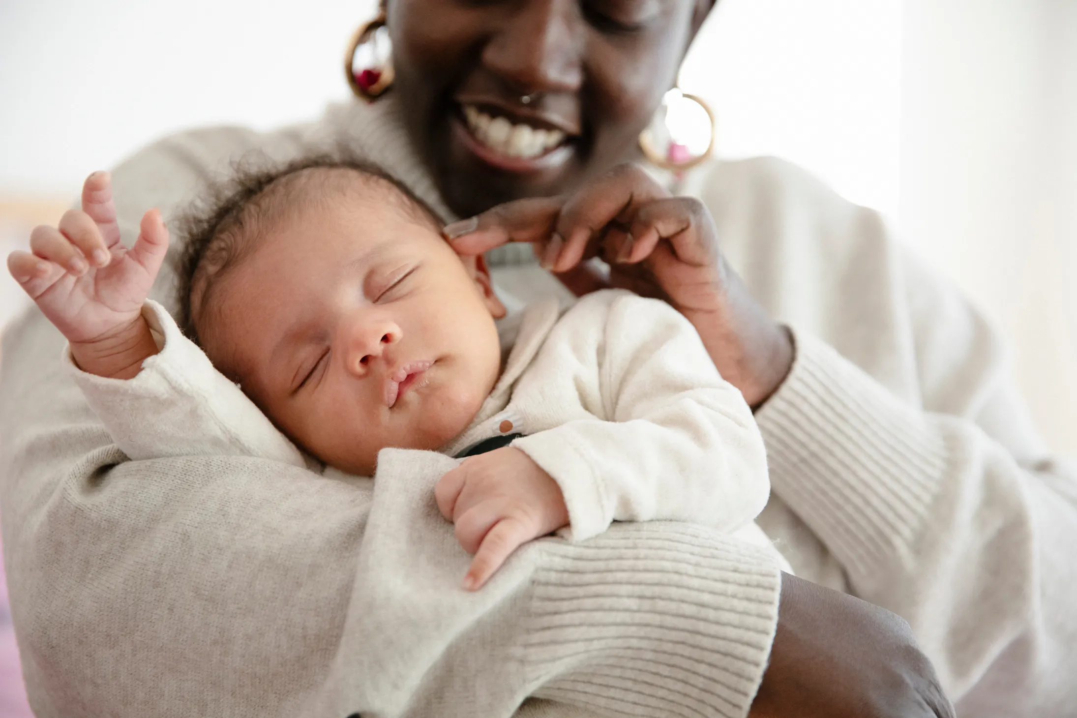 A smiling woman holding her sleeping newborn baby in her arms.